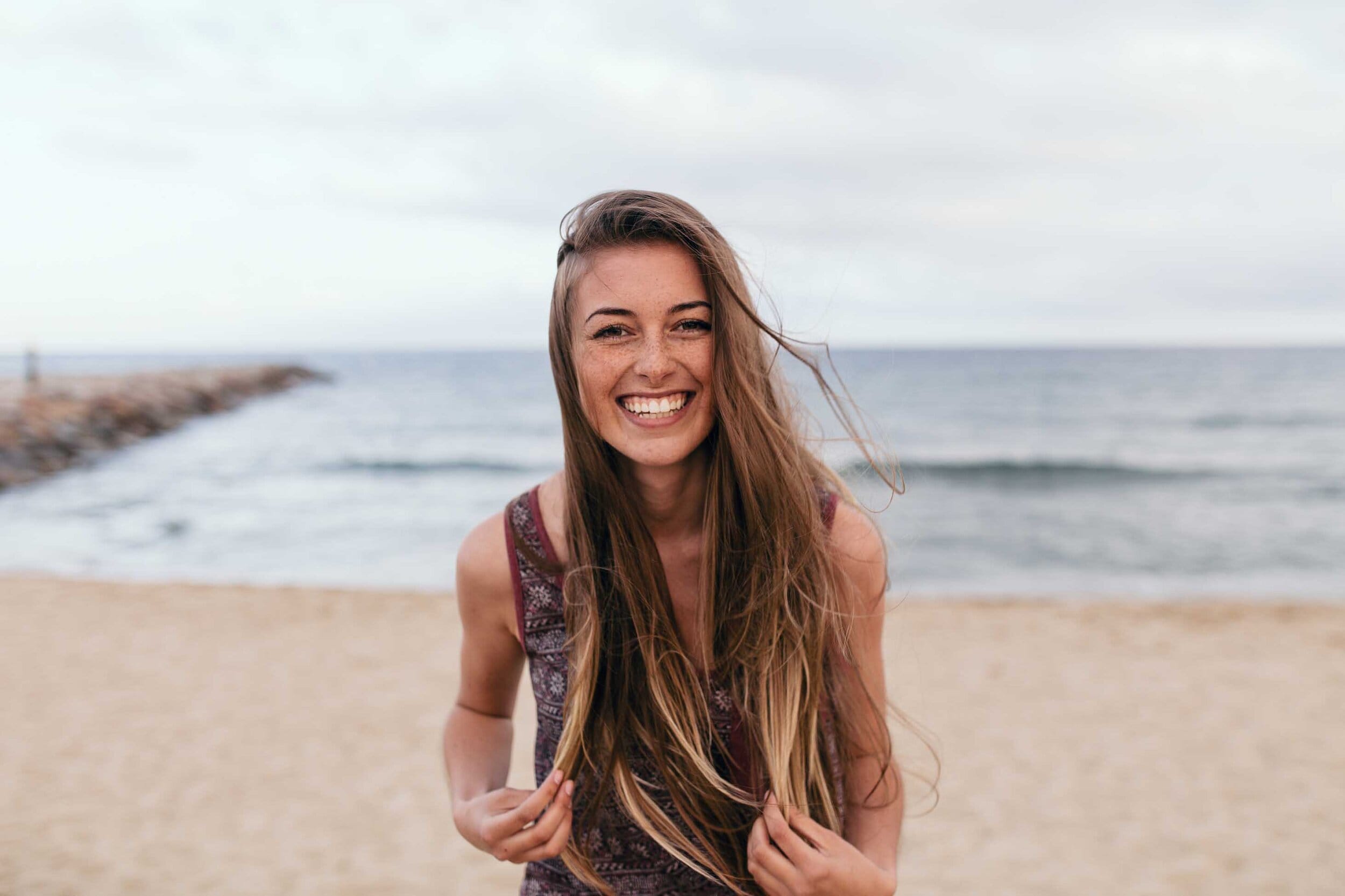 A smiling woman on a beach, showing the importance and results of mental health days on emotional stability.