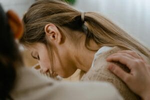 An emotional moment about the best treatment facilities for outpatient addiction help, showing a comforting gesture with a hand on a woman's shoulder.