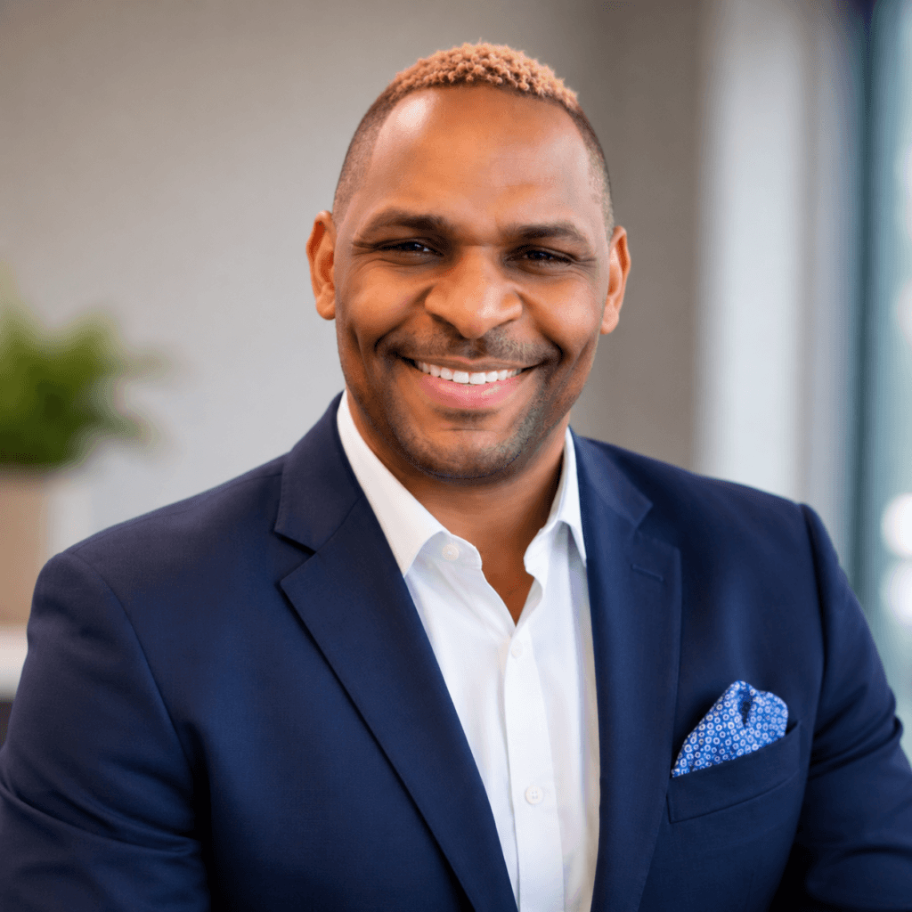 cedric A man in a navy suit and white shirt, possibly one of many substance abuse professionals, smiles while sitting indoors. He has short, light hair and a patterned pocket square. A plant and window are blurred in the background.