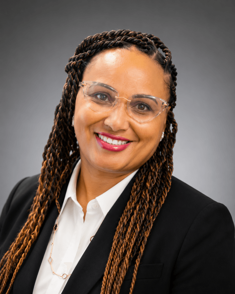 rachel A woman with long, braided hair, wearing glasses, a white shirt, and a black blazer, smiles at the camera against a gray background—reflecting the confidence often seen in experienced substance abuse professionals.